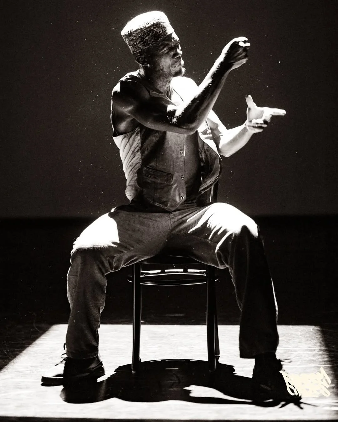 Black and white photo of Oulouy seated on a chair, performing.