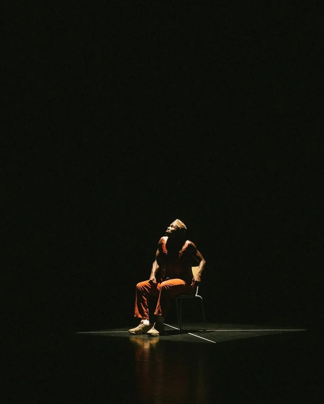 Dancer seated on a chair in a dark room.